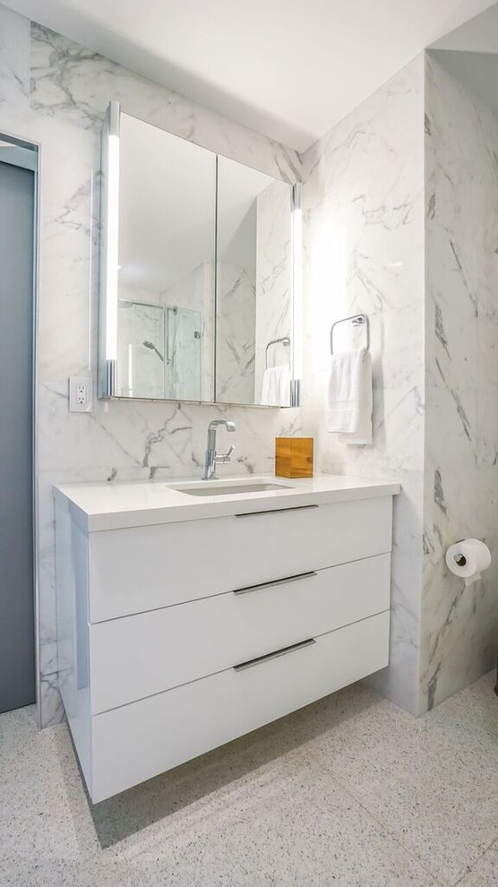Photo of a mid-sized contemporary bathroom in Miami with flat-panel cabinets, white cabinets, a shower/bathtub combo, white tile, stone tile, white walls, marble floors, an undermount sink and engineered quartz benchtops.