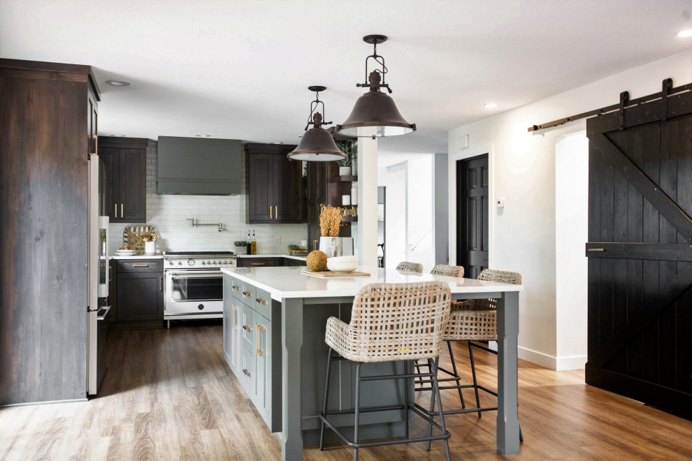 Design ideas for a large country l-shaped eat-in kitchen in Minneapolis with shaker cabinets, with island, white splashback, white appliances, medium hardwood floors, brown floor, white benchtop, quartz benchtops, subway tile splashback, a farmhouse sink and dark wood cabinets.