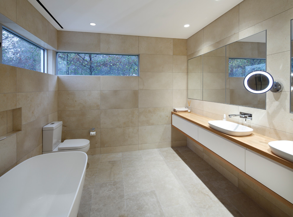 Inspiration for a mid-sized contemporary master bathroom in Wollongong with a freestanding tub, a two-piece toilet, beige tile, ceramic tile, beige walls, ceramic floors, a vessel sink, wood benchtops, beige floor and brown benchtops.