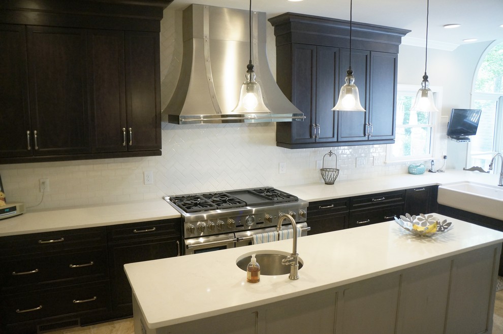 Example of a mid-sized transitional l-shaped travertine floor eat-in kitchen design in Raleigh with a farmhouse sink, flat-panel cabinets, dark wood cabinets, quartz countertops, white backsplash, ceramic backsplash, stainless steel appliances and an island