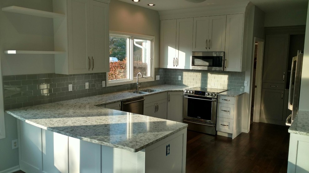 Mid-sized transitional u-shaped eat-in kitchen photo with an undermount sink, flat-panel cabinets, white cabinets, quartz countertops, gray backsplash, glass tile backsplash and stainless steel appliances