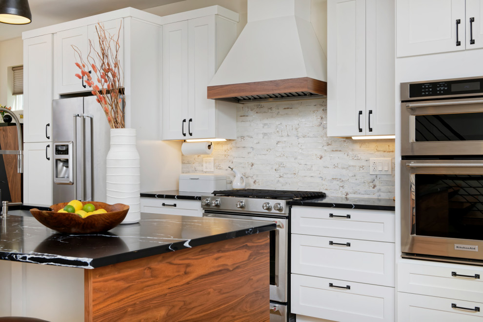 Design ideas for a mid-sized contemporary l-shaped eat-in kitchen in Denver with an undermount sink, shaker cabinets, white cabinets, granite benchtops, white splashback, stainless steel appliances, medium hardwood floors, with island and black benchtop.