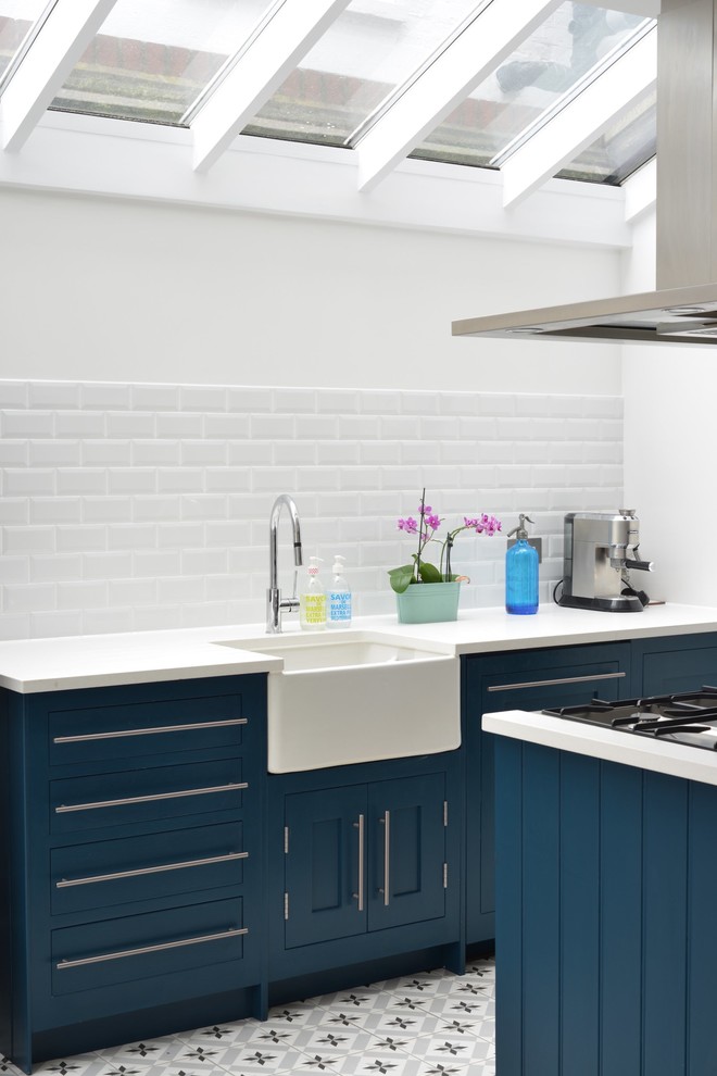 Inspiration for a mid-sized country kitchen in London with a farmhouse sink, blue cabinets, solid surface benchtops, white splashback, ceramic floors, flat-panel cabinets and subway tile splashback.