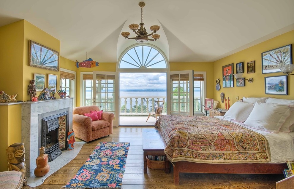 This is an example of a large eclectic master bedroom in Seattle with yellow walls, light hardwood floors, a standard fireplace, a concrete fireplace surround and beige floor.