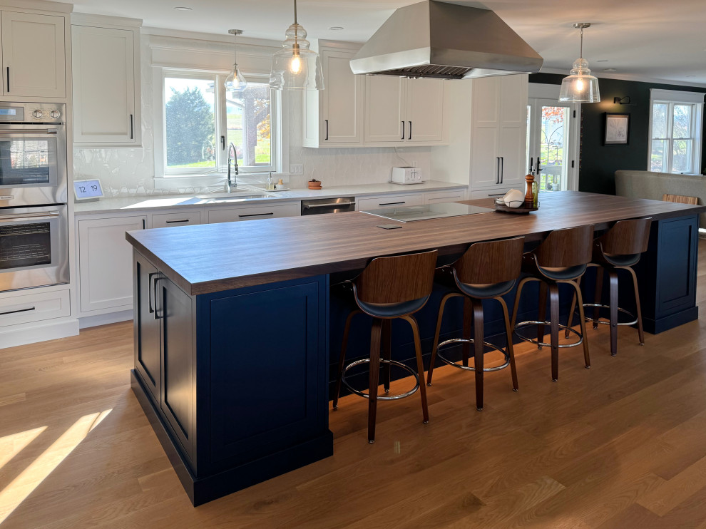 Example of a mid-sized transitional l-shaped medium tone wood floor and brown floor eat-in kitchen design with an undermount sink, shaker cabinets, blue cabinets, white backsplash, an island and brown countertops