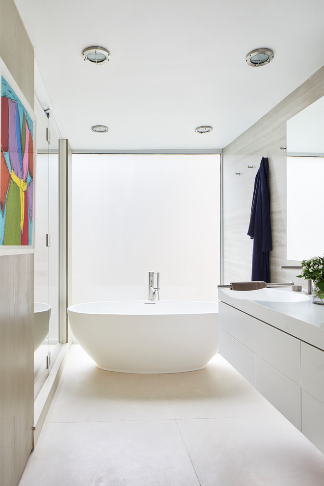 Contemporary master bathroom in New York with flat-panel cabinets, white cabinets, a freestanding tub, an alcove shower, beige walls, an integrated sink, beige floor and a hinged shower door.