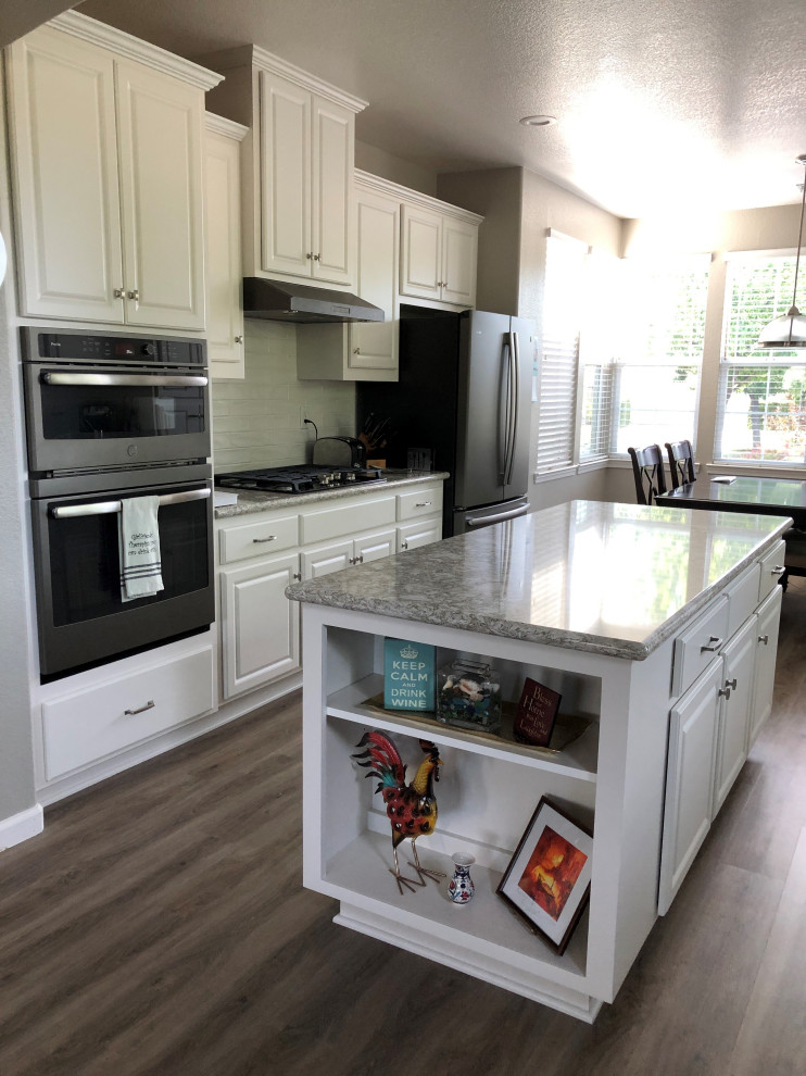 This is an example of a large transitional galley eat-in kitchen in Sacramento with an undermount sink, raised-panel cabinets, white cabinets, quartz benchtops, ceramic splashback, coloured appliances, vinyl floors, with island, brown floor, multi-coloured benchtop and beige splashback.