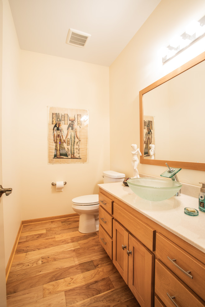 Inspiration for a small transitional 3/4 medium tone wood floor and brown floor bathroom remodel with shaker cabinets, medium tone wood cabinets, a two-piece toilet, beige walls, a vessel sink and white countertops