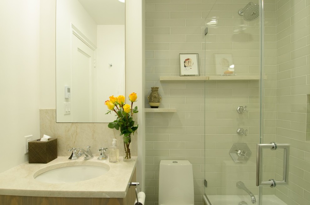 Photo of a small contemporary master bathroom in New York with flat-panel cabinets, medium wood cabinets, a drop-in tub, a shower/bathtub combo, a one-piece toilet, gray tile, glass tile, white walls, an undermount sink and quartzite benchtops.