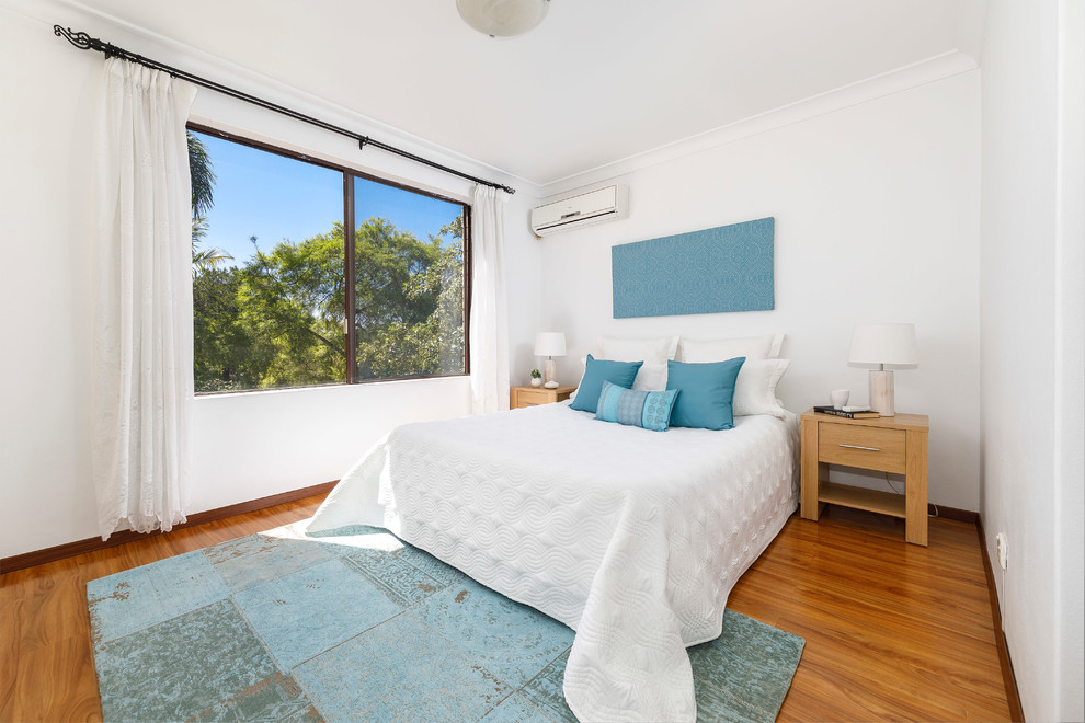 Beach style guest bedroom in Sydney with white walls, medium hardwood floors and brown floor.