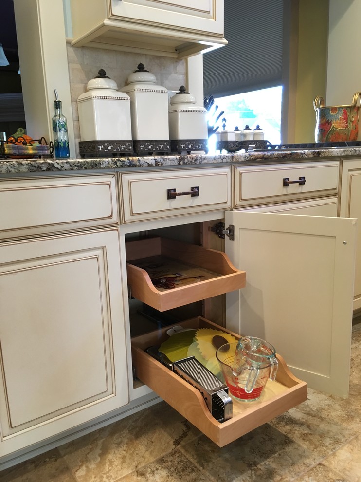 Large transitional galley porcelain tile enclosed kitchen photo with an undermount sink, raised-panel cabinets, distressed cabinets, granite countertops, beige backsplash, stone tile backsplash, stainless steel appliances and a peninsula