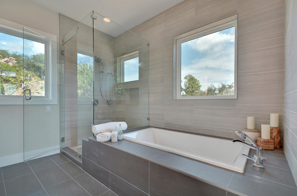 This is an example of a large contemporary master bathroom in Austin with shaker cabinets, medium wood cabinets, a drop-in tub, a corner shower, a one-piece toilet, gray tile, porcelain tile, grey walls, porcelain floors, an undermount sink, engineered quartz benchtops, grey floor and a hinged shower door.