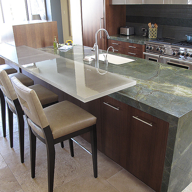 Photo of a large modern kitchen in San Diego with an undermount sink, flat-panel cabinets, dark wood cabinets, marble benchtops, grey splashback, porcelain splashback, stainless steel appliances, limestone floors, with island and brown floor.