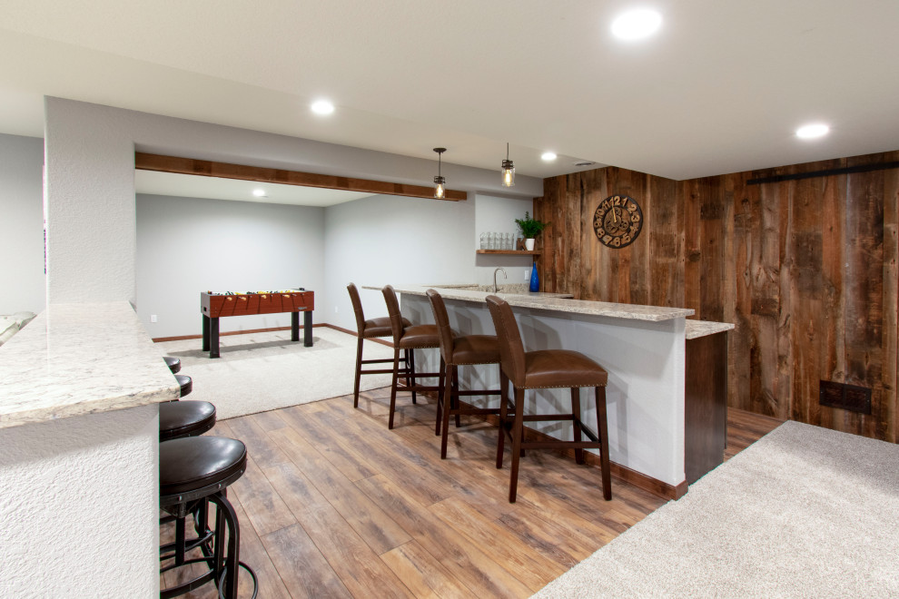 Expansive transitional fully buried basement in Milwaukee with a home bar, grey walls, carpet, beige floor, exposed beam and wood walls.