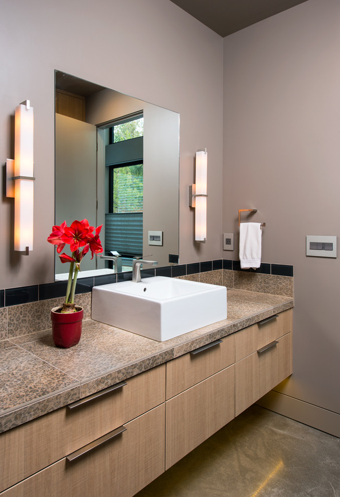 Photo of a mid-sized contemporary master bathroom in Other with a vessel sink, flat-panel cabinets, light wood cabinets, granite benchtops, grey walls, concrete floors, a corner shower and a one-piece toilet.