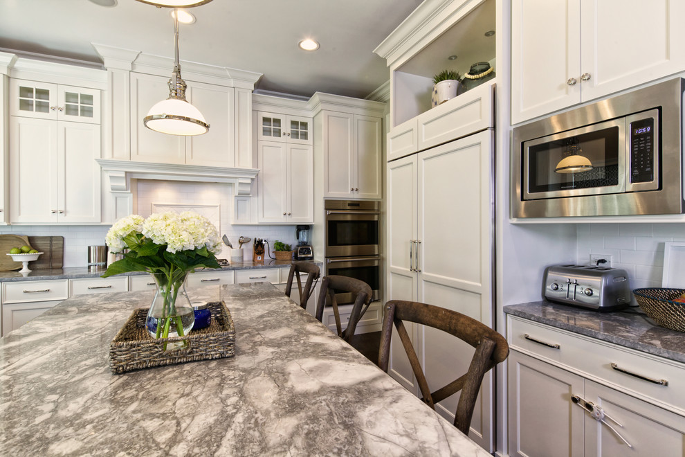 Photo of a large beach style l-shaped eat-in kitchen in Chicago with shaker cabinets, white cabinets, marble benchtops, white splashback, subway tile splashback, stainless steel appliances, dark hardwood floors and with island.