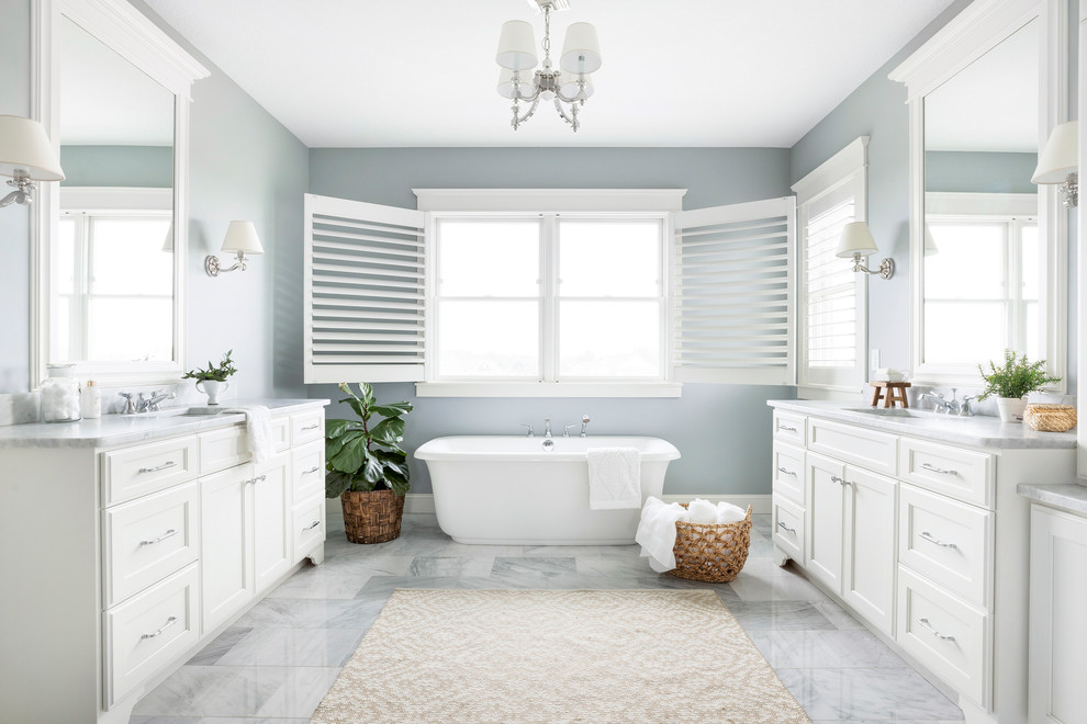 Beach style master bathroom in Minneapolis with recessed-panel cabinets, white cabinets, a freestanding tub, grey walls, marble floors, an undermount sink, grey floor, grey benchtops and marble benchtops.