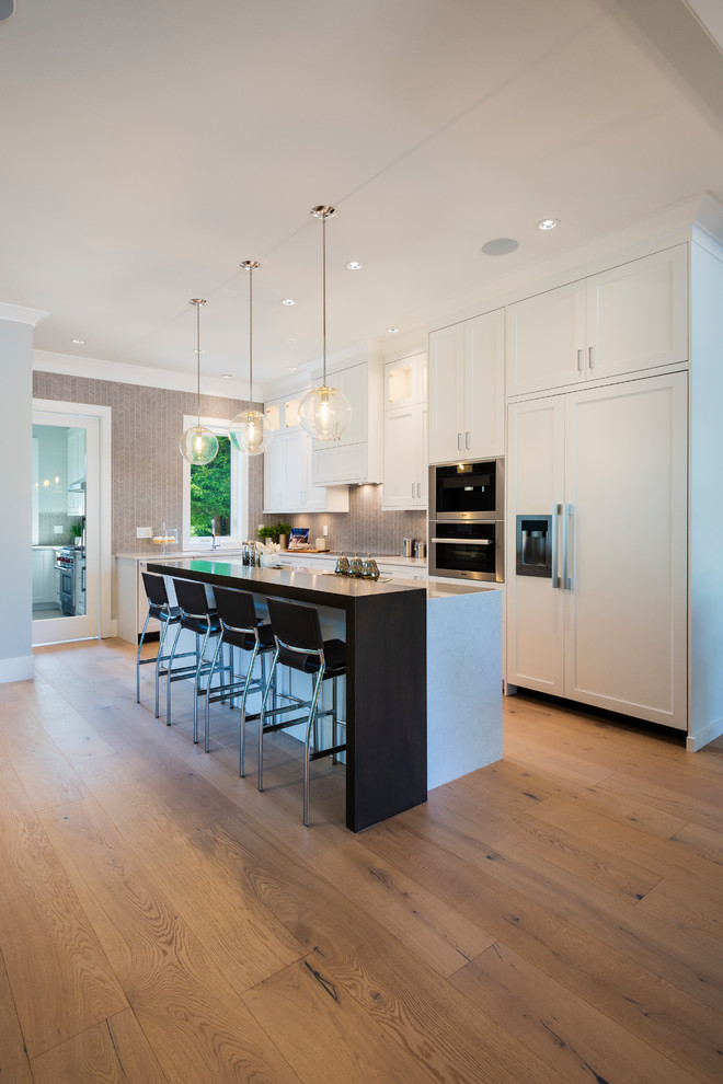 Example of a mid-sized transitional l-shaped light wood floor and beige floor open concept kitchen design in Vancouver with an undermount sink, shaker cabinets, white cabinets, quartz countertops, gray backsplash, mosaic tile backsplash, paneled appliances, an island and gray countertops