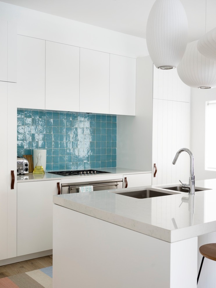 Inspiration for a beach style kitchen in Sydney with flat-panel cabinets, white cabinets, blue splashback and with island.