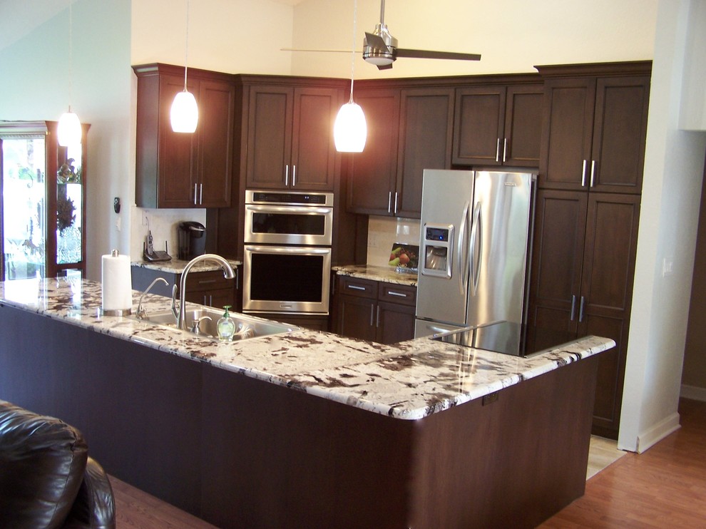 Kitchen - transitional travertine floor kitchen idea in Tampa with an undermount sink, recessed-panel cabinets, dark wood cabinets, granite countertops, white backsplash, ceramic backsplash, stainless steel appliances and white walls
