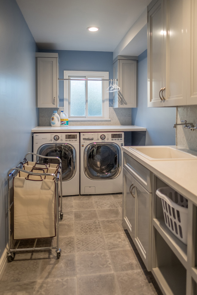 Design ideas for a mid-sized transitional galley dedicated laundry room in Los Angeles with a single-bowl sink, shaker cabinets, grey cabinets, quartz benchtops, blue walls, ceramic floors, a side-by-side washer and dryer and grey floor.