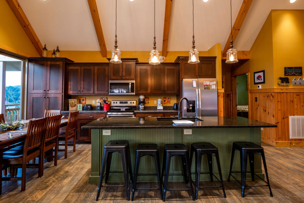 Example of a mid-sized mountain style laminate floor and brown floor kitchen design with shaker cabinets, brown cabinets, granite countertops, gray backsplash, an island and gray countertops