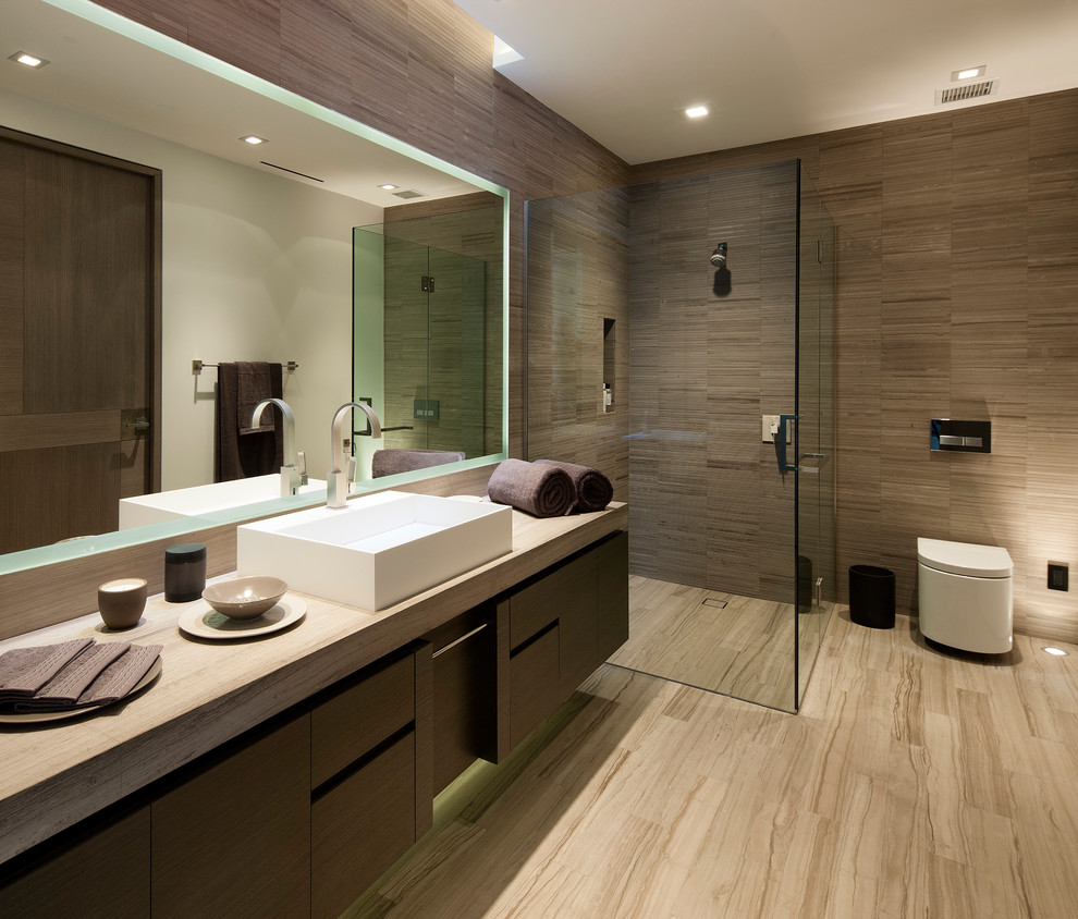 This is an example of a contemporary bathroom in Los Angeles with a vessel sink, flat-panel cabinets, dark wood cabinets, a curbless shower, a wall-mount toilet, brown tile and beige floor.