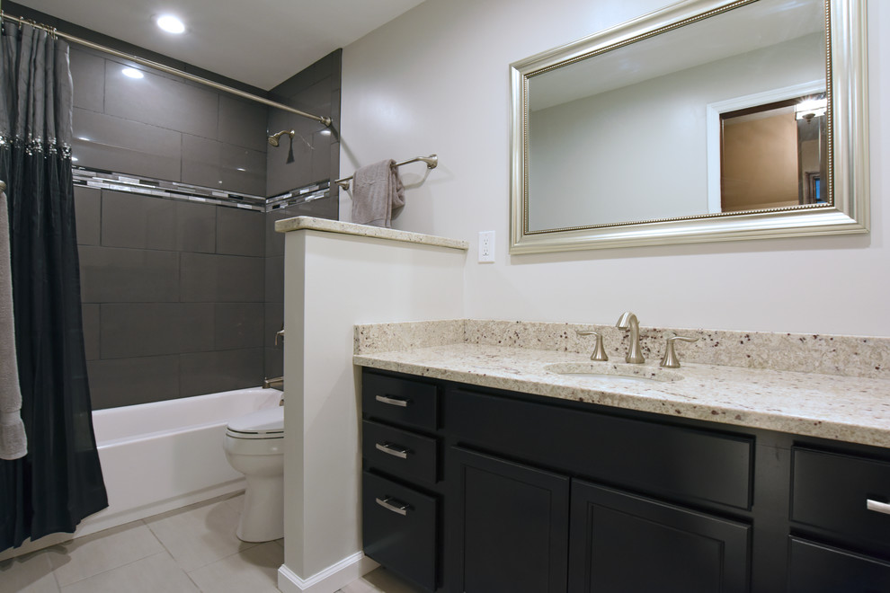 Photo of a contemporary bathroom in Other with recessed-panel cabinets, black cabinets, a drop-in tub, a shower/bathtub combo, gray tile, porcelain tile, white walls, porcelain floors, an undermount sink, granite benchtops, beige floor and a shower curtain.