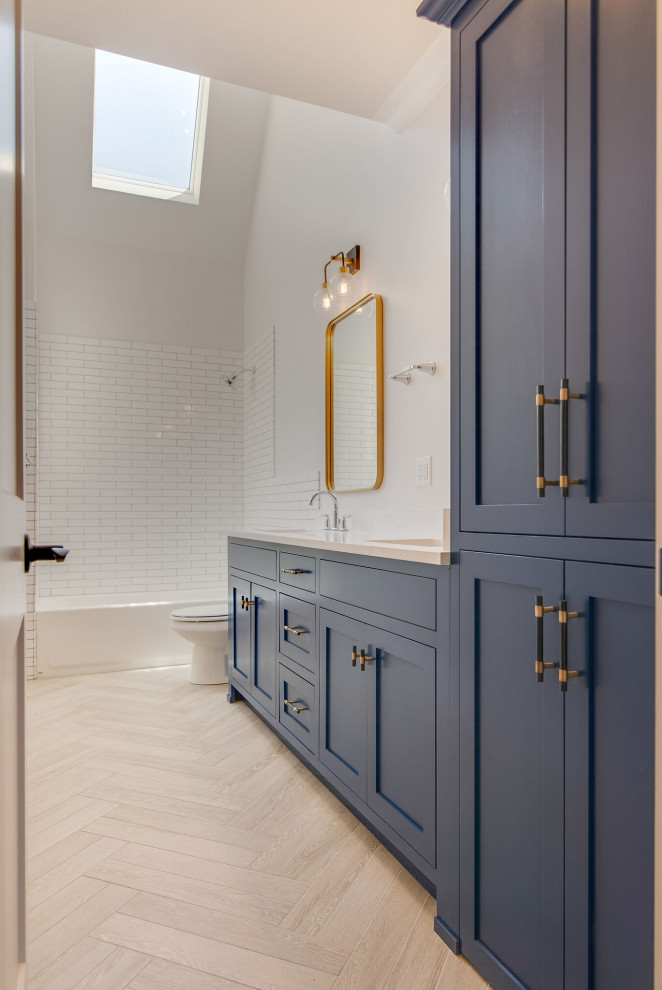 Photo of a medium sized classic family bathroom in Nashville with shaker cabinets, blue cabinets, an alcove bath, a two-piece toilet, white tiles, metro tiles, white walls, wood-effect flooring, a submerged sink, engineered stone worktops, beige floors, white worktops, a single sink, a built in vanity unit and a vaulted ceiling.