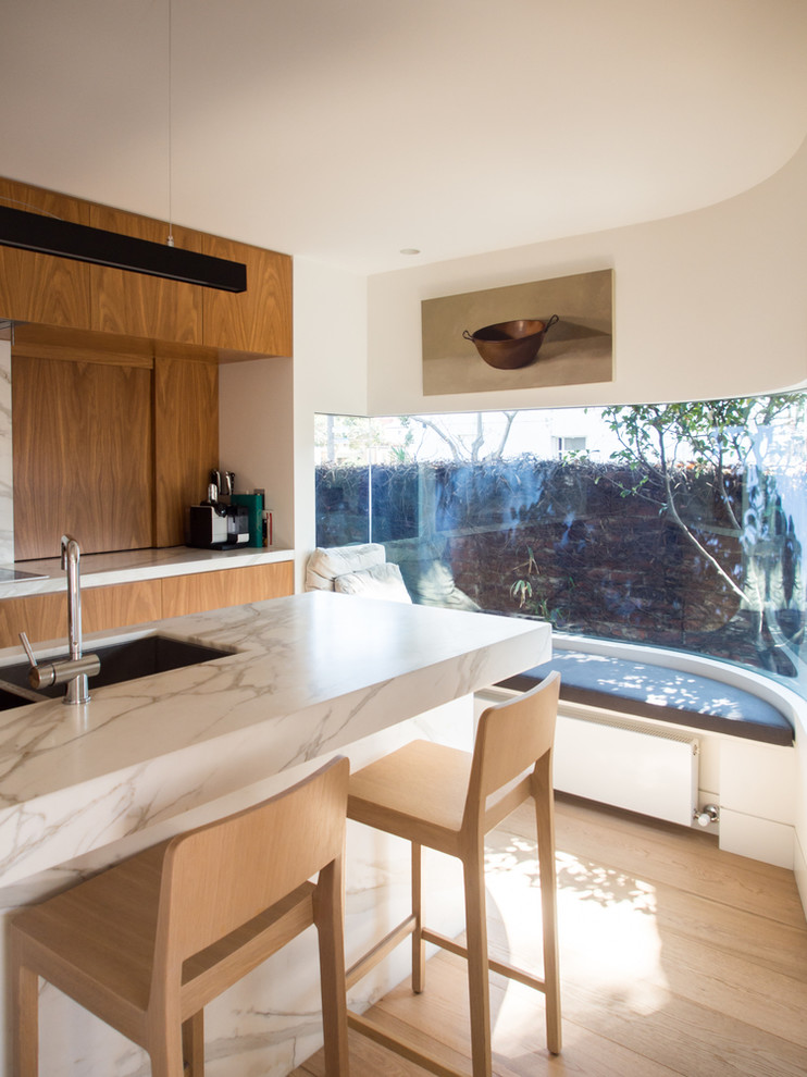 This is an example of a contemporary kitchen in Melbourne with light hardwood floors and marble benchtops.
