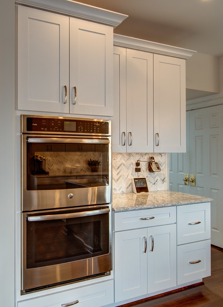 Example of a mid-sized transitional u-shaped dark wood floor and brown floor eat-in kitchen design in DC Metro with a farmhouse sink, shaker cabinets, white cabinets, stainless steel appliances, an island, gray countertops, quartzite countertops, white backsplash and mosaic tile backsplash
