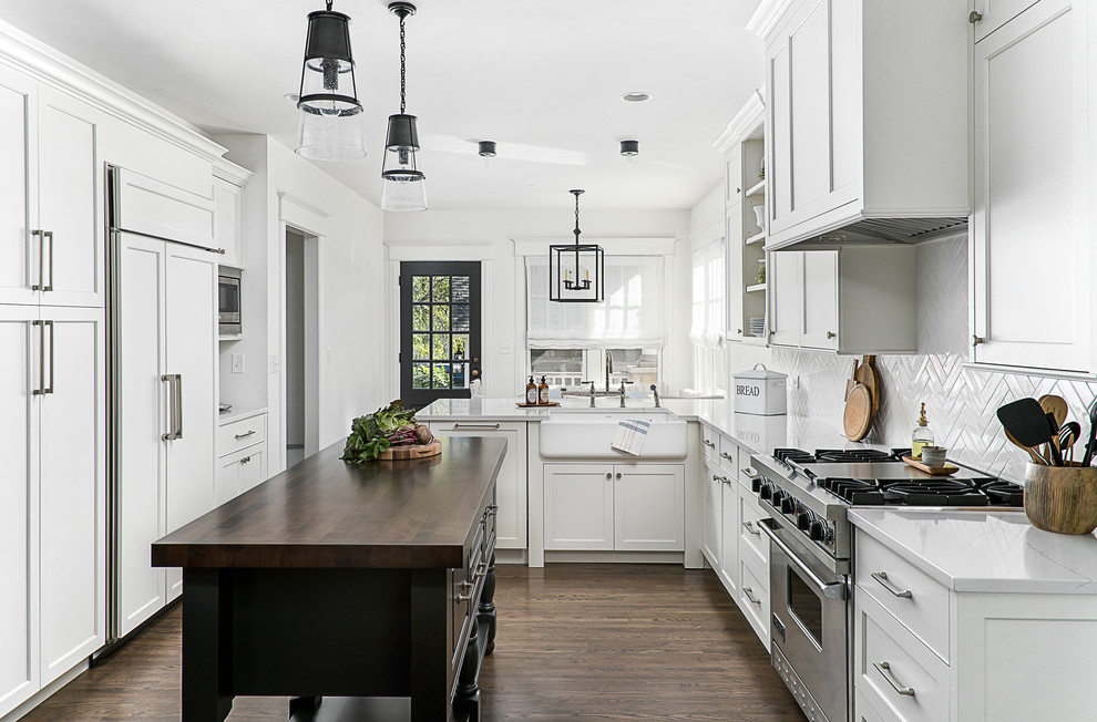 Photo of a mid-sized traditional u-shaped eat-in kitchen in Chicago with a farmhouse sink, shaker cabinets, white cabinets, quartz benchtops, white splashback, porcelain splashback, stainless steel appliances, dark hardwood floors, brown floor and with island.