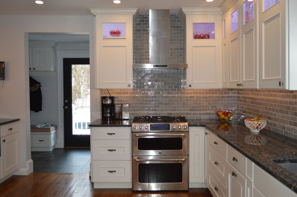 Example of a mid-sized transitional l-shaped medium tone wood floor eat-in kitchen design in Boston with an undermount sink, recessed-panel cabinets, white cabinets, granite countertops, gray backsplash, cement tile backsplash, stainless steel appliances, a peninsula and blue countertops