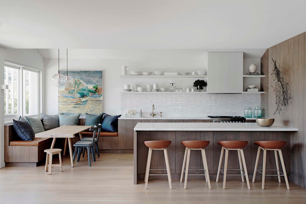 Beach style galley eat-in kitchen in Sydney with white splashback, light hardwood floors and a peninsula.