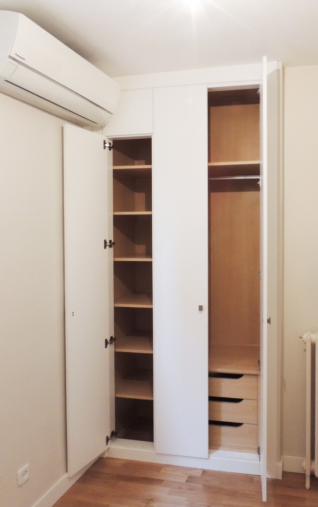 Small contemporary gender-neutral walk-in wardrobe in Madrid with flat-panel cabinets, white cabinets and medium hardwood floors.