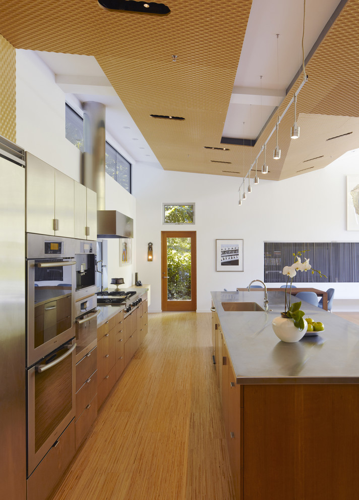 Photo of a mid-sized modern open plan kitchen in San Francisco with an integrated sink, stainless steel benchtops, flat-panel cabinets, stainless steel appliances, medium wood cabinets, light hardwood floors and with island.