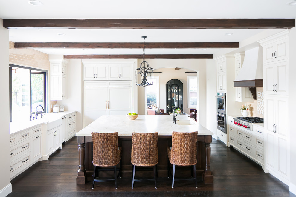 Mediterranean separate kitchen in San Diego with panelled appliances, dark hardwood floors, with island, a farmhouse sink, recessed-panel cabinets, white cabinets, brown floor and white benchtop.