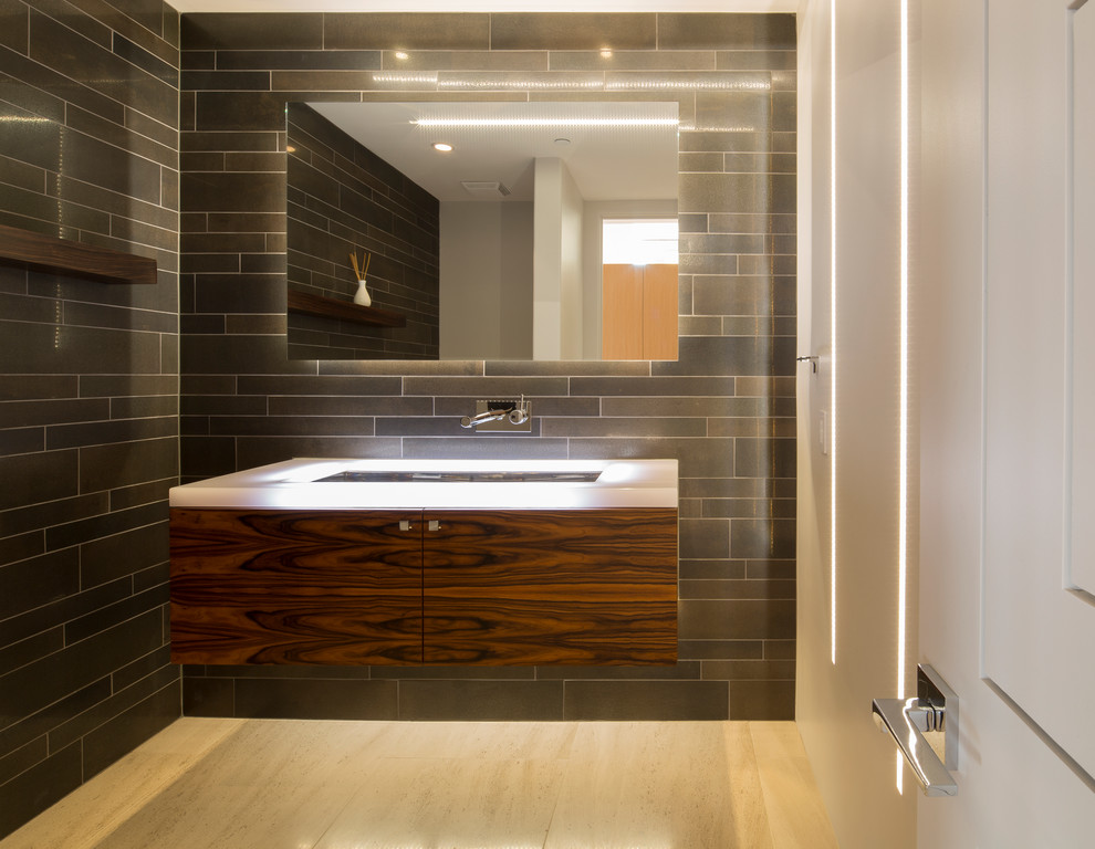 Inspiration for a mid-sized contemporary powder room in Phoenix with flat-panel cabinets, dark wood cabinets, a one-piece toilet, gray tile, ceramic tile, grey walls, porcelain floors, a wall-mount sink, engineered quartz benchtops, beige floor and white benchtops.