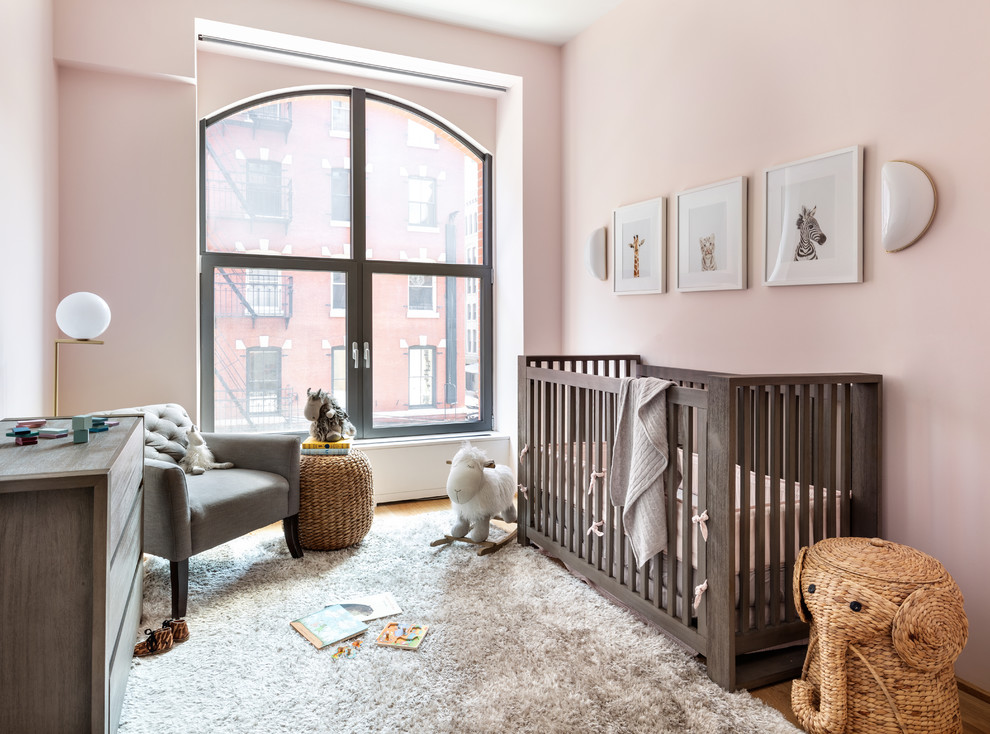Inspiration for a mid-sized contemporary nursery for girls in New York with pink walls, light hardwood floors and beige floor.