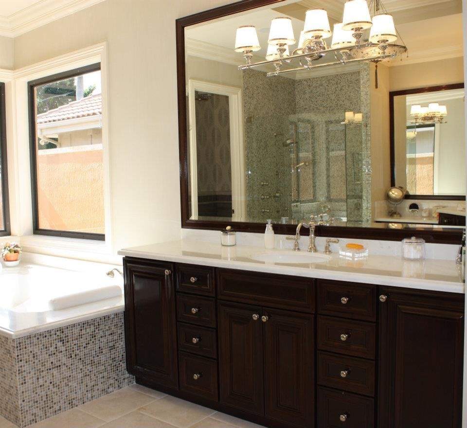 This is an example of a large traditional master bathroom in Miami with raised-panel cabinets, an undermount sink, dark wood cabinets, a corner tub, an alcove shower, multi-coloured tile, beige walls and marble floors.