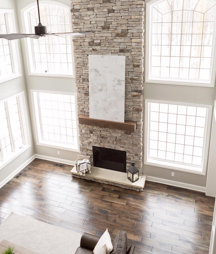 Cette image montre un salon avec parquet foncé, une cheminée double-face, un manteau de cheminée en pierre de parement et un téléviseur fixé au mur.