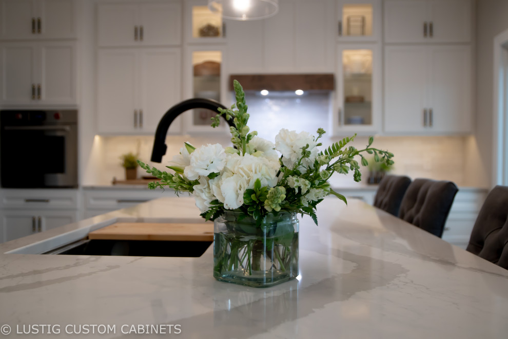 Inspiration for a large transitional l-shaped laminate floor and brown floor open concept kitchen remodel with an undermount sink, flat-panel cabinets, white cabinets, quartz countertops, white backsplash, ceramic backsplash, stainless steel appliances, an island and white countertops