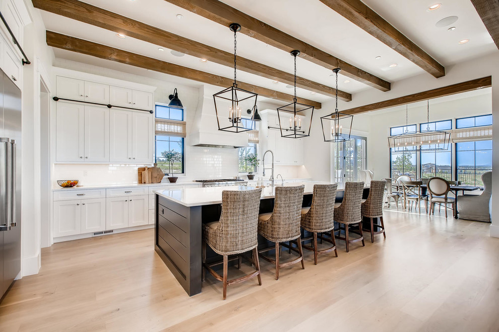 Inspiration for a large country galley kitchen in Denver with a farmhouse sink, shaker cabinets, white cabinets, quartz benchtops, white splashback, subway tile splashback, stainless steel appliances, light hardwood floors, with island, white benchtop and beige floor.