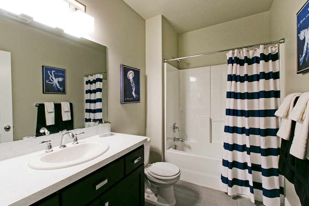 Photo of a mid-sized arts and crafts 3/4 bathroom in Salt Lake City with a drop-in sink, recessed-panel cabinets, black cabinets, laminate benchtops, a drop-in tub, a one-piece toilet, gray tile, ceramic tile, white walls, ceramic floors, a shower/bathtub combo, grey floor, a shower curtain and white benchtops.