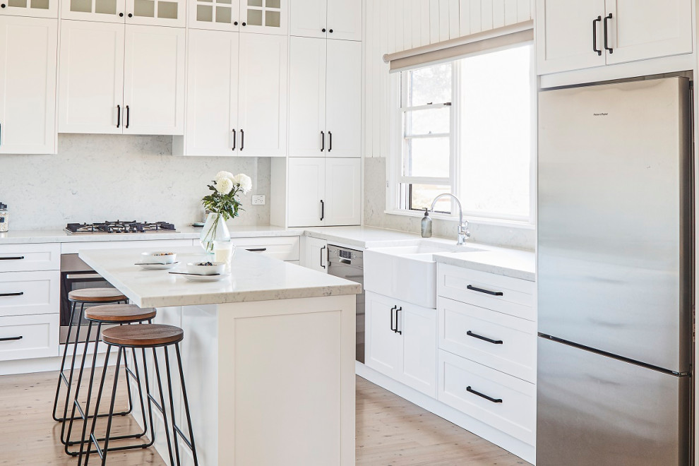 Transitional l-shaped kitchen in Sydney with quartz benchtops, a farmhouse sink, shaker cabinets, white cabinets, light hardwood floors, with island, beige floor and white benchtop.