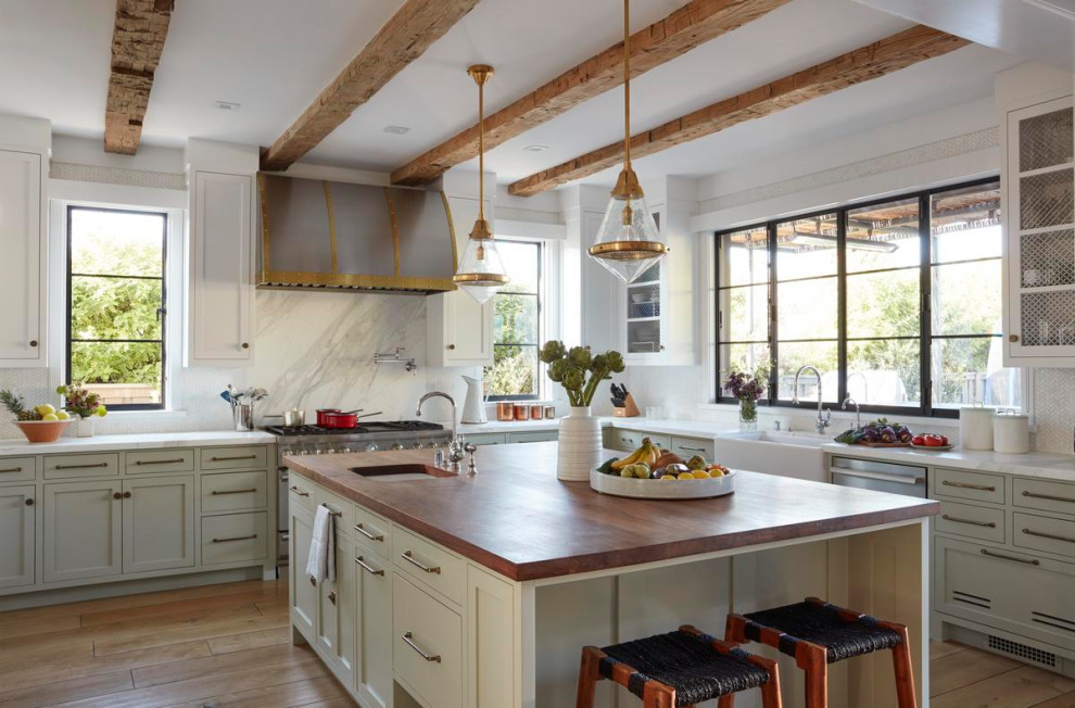 Design ideas for a country l-shaped kitchen in Los Angeles with a farmhouse sink, shaker cabinets, grey cabinets, white splashback, stone slab splashback, stainless steel appliances, medium hardwood floors, with island, brown floor, white benchtop and exposed beam.