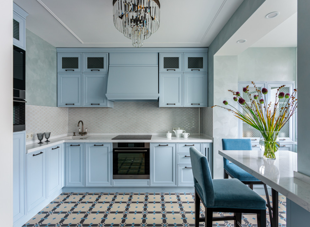 Photo of a small transitional l-shaped kitchen in Moscow with an undermount sink, quartz benchtops, stainless steel appliances, porcelain floors, multi-coloured floor, white benchtop, recessed-panel cabinets, blue cabinets, grey splashback, mosaic tile splashback and a peninsula.