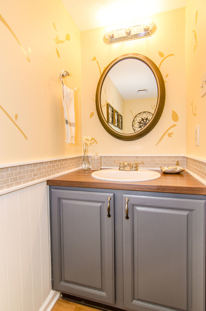 Inspiration for a mid-sized transitional powder room in Philadelphia with a drop-in sink, raised-panel cabinets, grey cabinets, laminate benchtops, a one-piece toilet, beige tile, ceramic tile, yellow walls and medium hardwood floors.