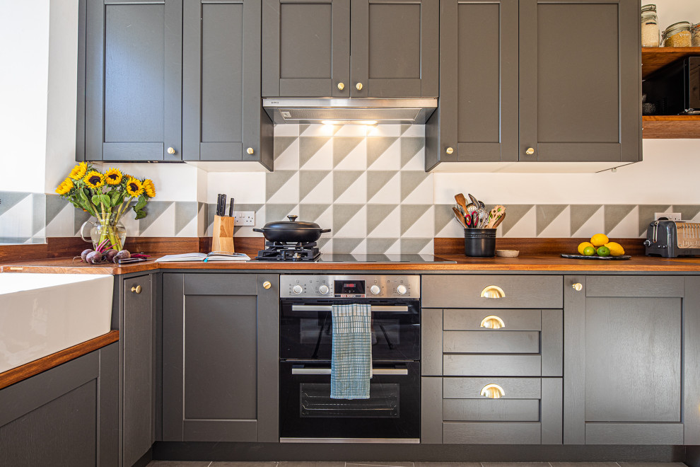 Photo of a small traditional l-shaped eat-in kitchen in Other with a farmhouse sink, shaker cabinets, grey cabinets, wood benchtops, grey splashback, panelled appliances, ceramic floors, no island, grey floor and brown benchtop.