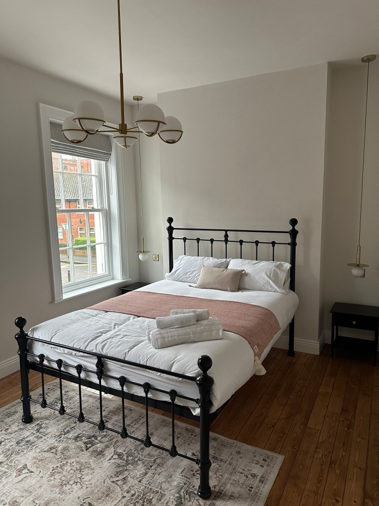 Modelo de habitación de invitados vintage grande sin chimenea con paredes blancas, suelo de madera en tonos medios y suelo marrón